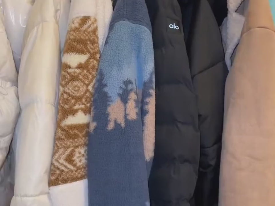 Bulky winter coats being forced into a stuffed suitcase